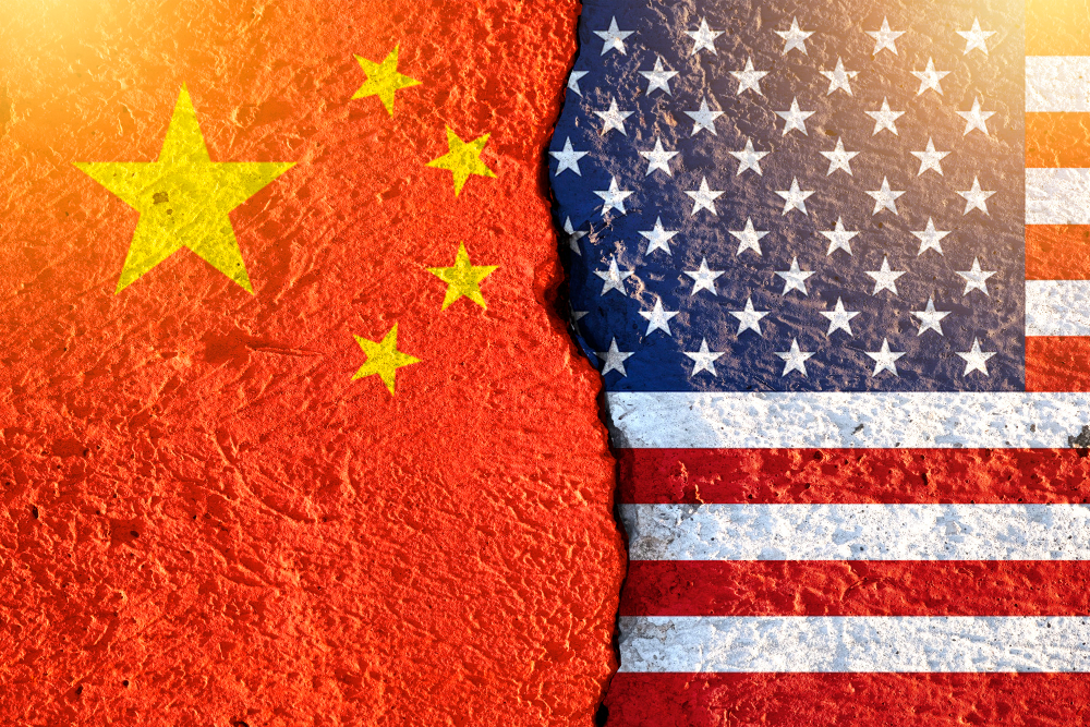 Bandeiras da China e dos Estados Unidos lado a lado em um muro rachado, simbolizando a tensão geopolítica envolvendo o roubo de bilhões em Bitcoin.