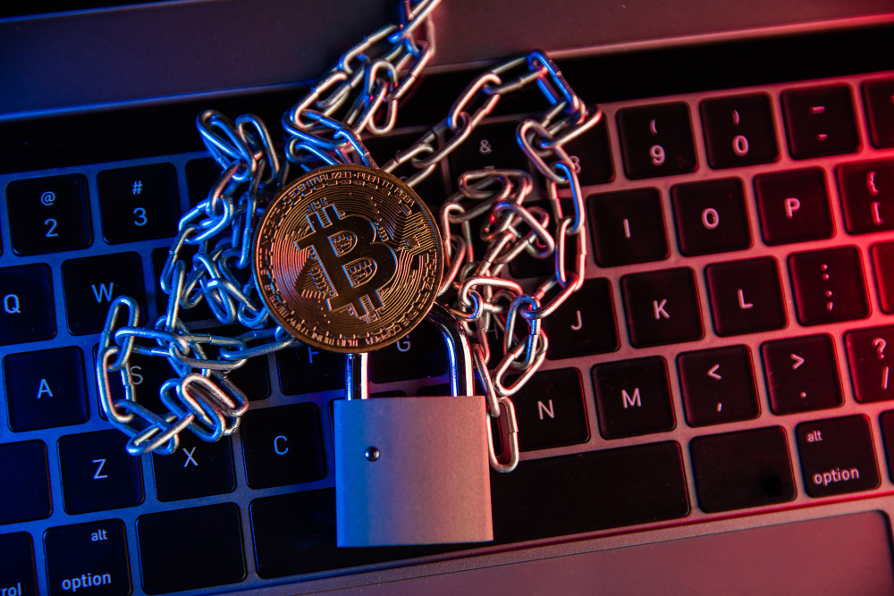 Moeda de Bitcoin presa por correntes e cadeado sobre teclado, simbolizando investigações de crimes com criptomoedas.