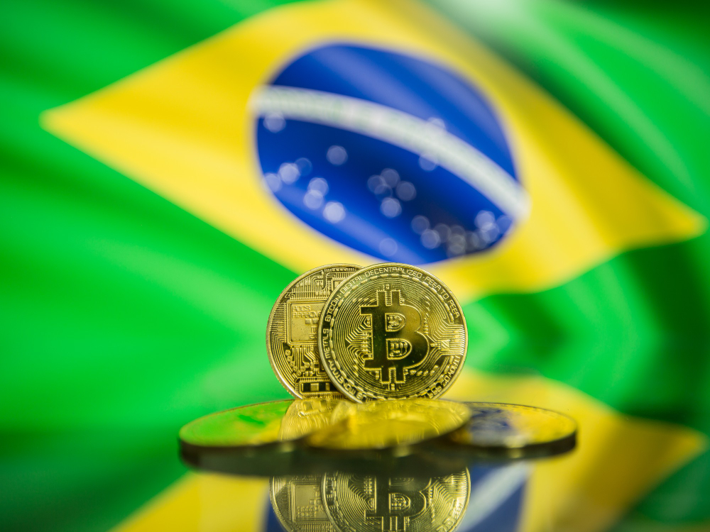 Moedas de Bitcoin sobre fundo da bandeira do Brasil, representando a atualização das regras de criptoativos pela Receita Federal.