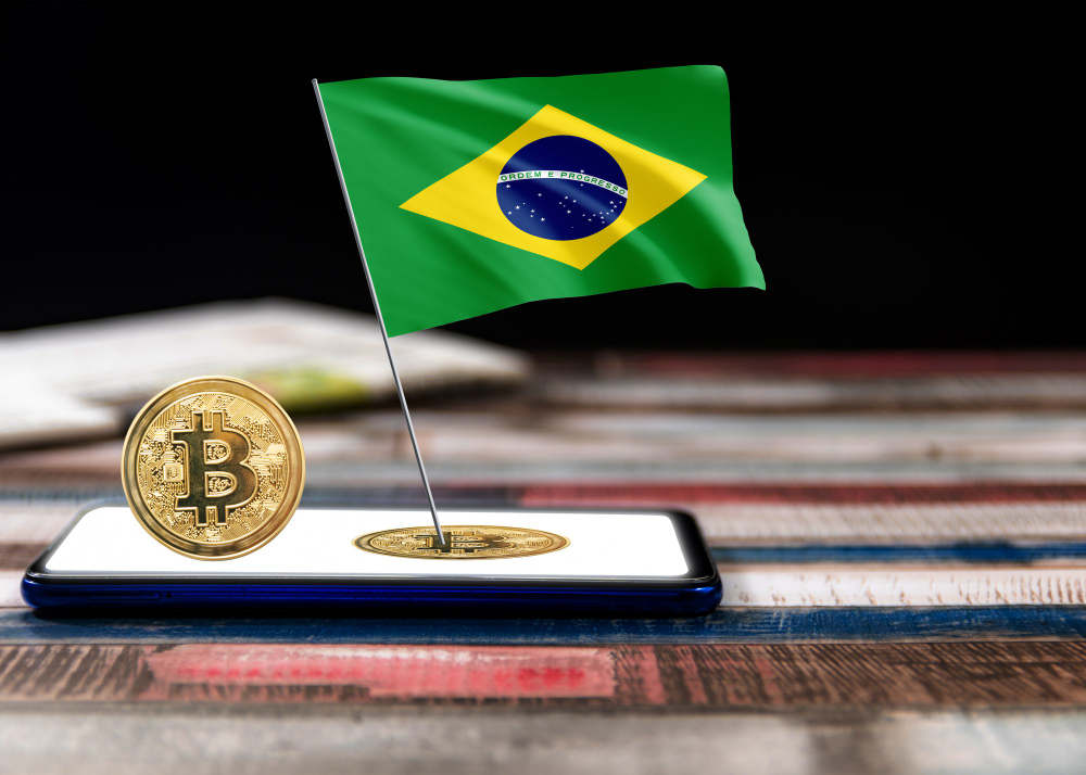 Moeda de Bitcoin e bandeira do Brasil sobre um smartphone, representando o debate regulatório sobre stablecoins e criptomoedas no país.
